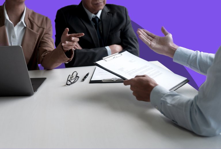 Two people sitting across the table from one person holding some documents and gesturing.