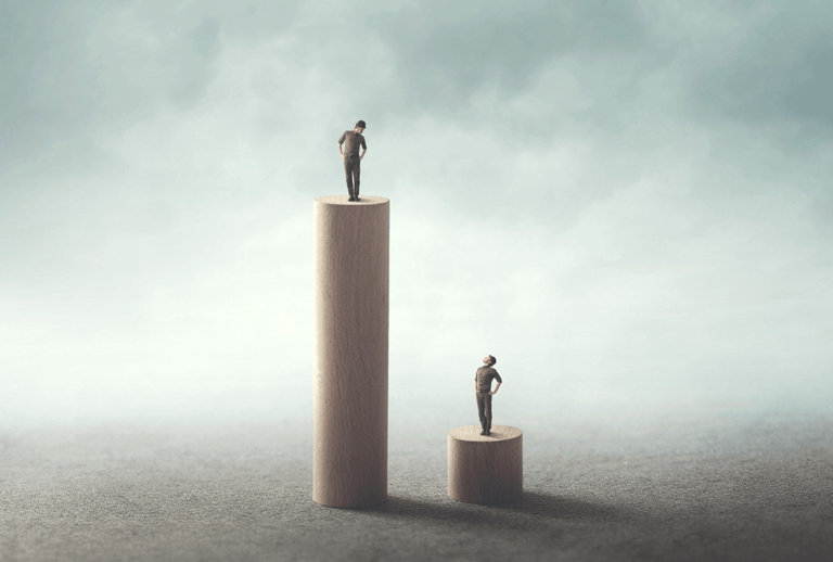 One person standing on a tall totem pole and another person standing on a short totem pole