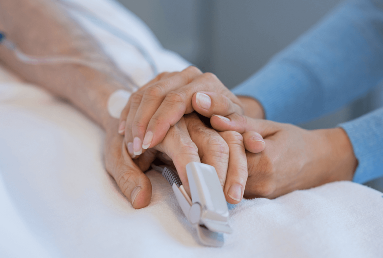 An elderly hand with a finger monitor being held by a younger looking hand