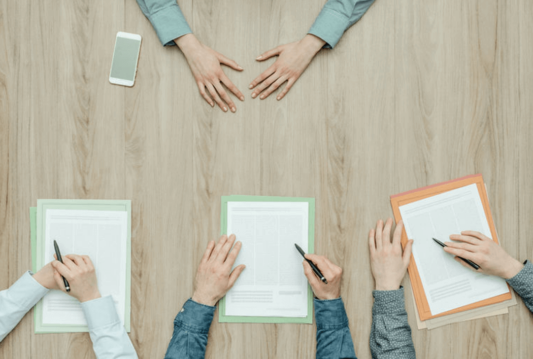 Overview image of 3 people with documents in front of them across the table from someone with their hands resting in front of them on the table
