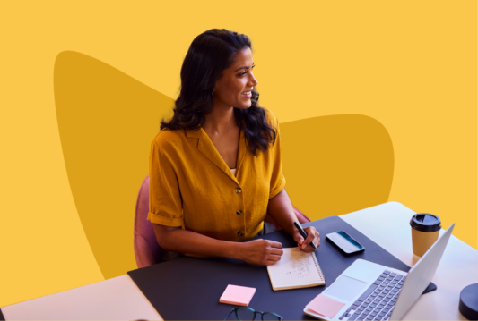 Woman smiling while writing on a notepad at her desk.