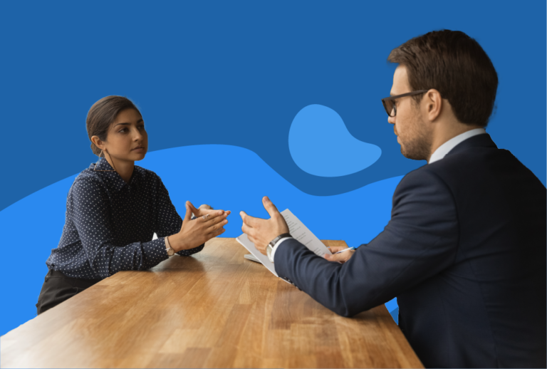 A senior employee holding paper and speaking with another employee across the table.