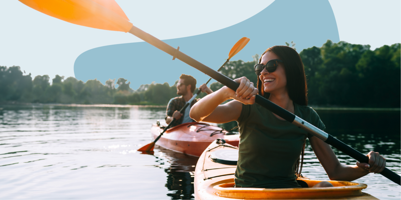 Two people paddling in kayaks in a lake surrounded by trees.