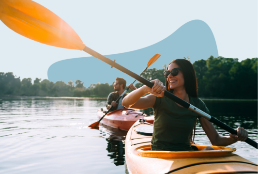 Two people paddling in kayaks in a lake surrounded by trees.