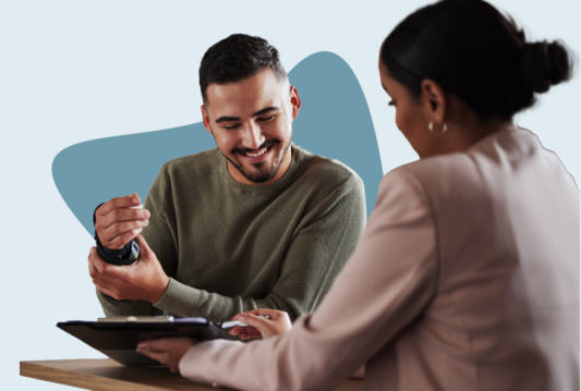 Employee holds a wrist brace on his right hand with his left hand while reviewing a clipboard with a manager in a pink blazer.