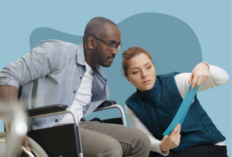 Red-haired woman crouching down holding up a blue report to a man in a wheelchair.