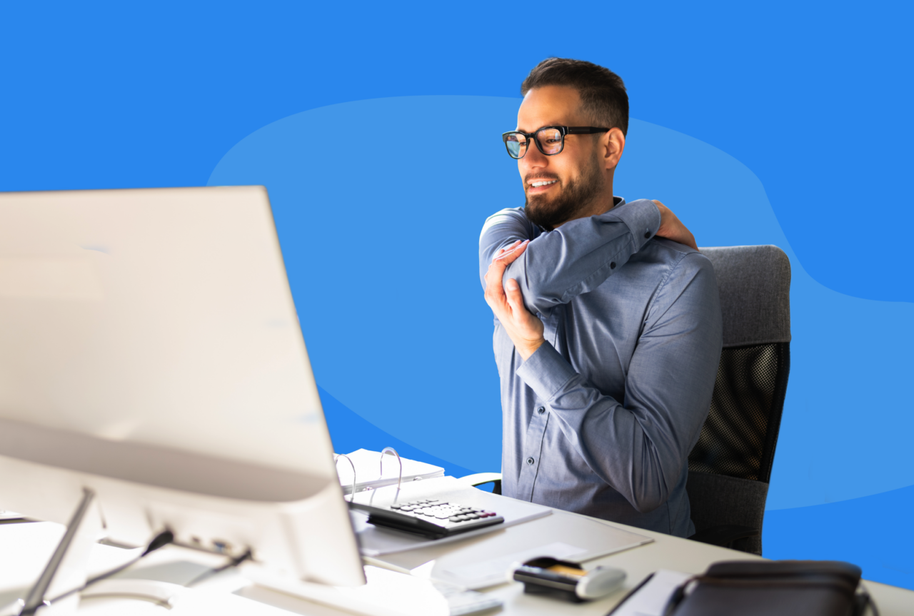 Employee sitting at a desk in front of a computer monitor rubbing his left shoulder.