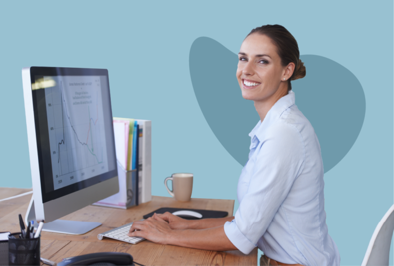Employee facing camera smiling while typing on a wireless keyboard in front of a computer monitor with graphs on it.