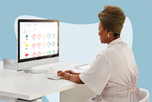 A woman is looking at a computer monitor on her desk, on the computer screen are sentiment analysis pie charts.