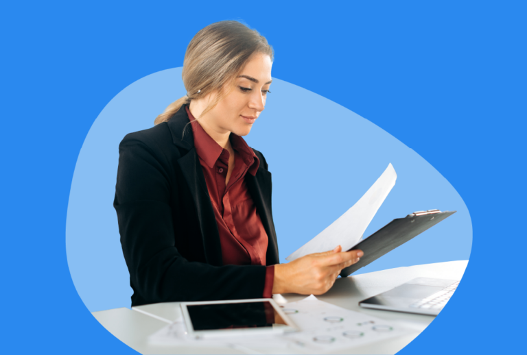 A woman is at her desk looking at a clipboard and paper